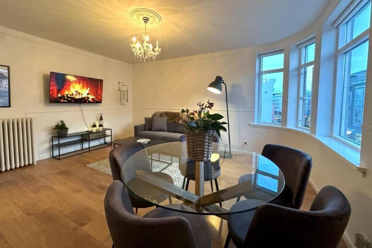 Ein modernes Wohnzimmer mit einem Glastisch, bequemen Sitzmöglichkeiten, einem Kamin und großen Fenstern.