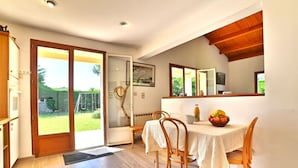 A dining area with a table set for two, a wooden floor, and a view of the garden through a glass door. - Beautiful private villa for 9 people with WIFI, TV and terrace (Saint-denis-d'oléron)