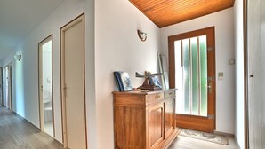 A hallway with wooden flooring, white walls, and a wooden ceiling. There is a wooden cabinet with a decorative item on top, a door with a frosted glass panel, and a light fixture on the wall. - Beautiful private villa for 9 people with WIFI, TV and terrace (Saint-denis-d'oléron)