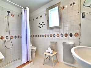 A bathroom with a shower, toilet, sink, and a window.