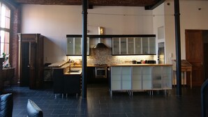 A modern kitchen with dark tiles, a central island, and a brick ceiling. - Luxury loft in Lille/Tourcoing with sauna, spa, 4 guests, with parking (Tourcoing)
