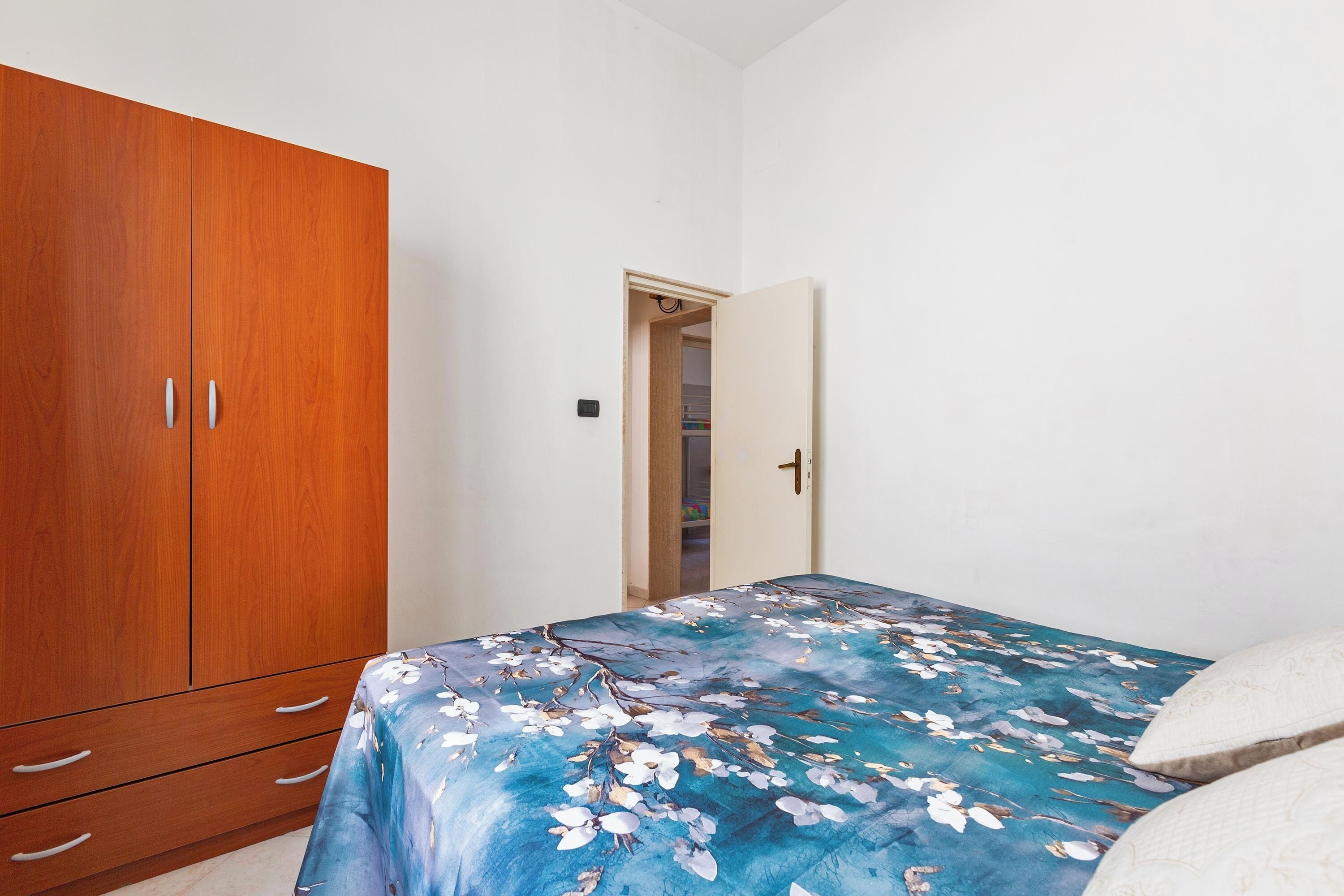 Ein Schlafzimmer mit einem Holzschrank, einem Bett mit floralem Überwurf und einer Tür zu einem Kleiderschrank.