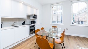 Moderni keittiö, jossa on valkoiset kaapit, lasinen ruokapöytä ja oranssit tuolit.