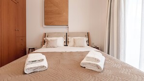 Un letto ben rifatto con una coperta beige, due asciugamani arrotolati e una testiera in legno.