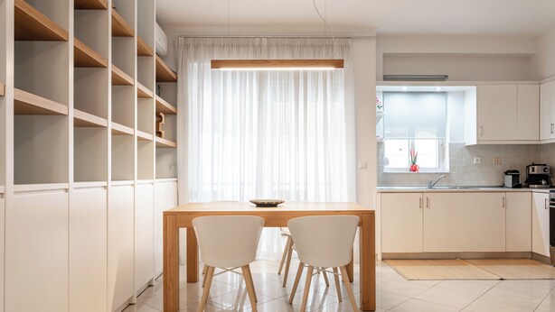 Una cucina moderna con mobili bianchi, un tavolo da pranzo in legno e due sedie bianche.