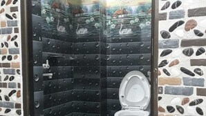 Un baño con pared de mosaicos, un inodoro y un cubo verde.