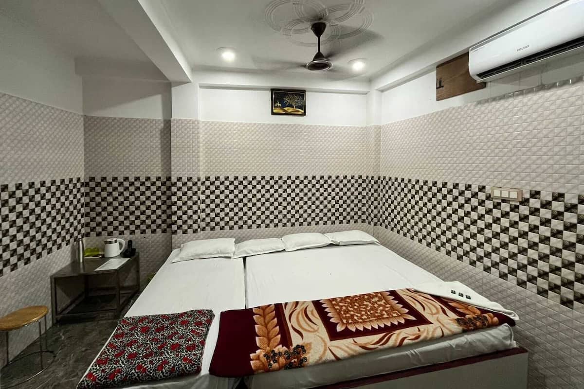 Una habitación de hotel con un patrón de pared a cuadros, una cama con colcha estampada, una mesita de noche con una taza y un libro, y un ventilador de techo.
