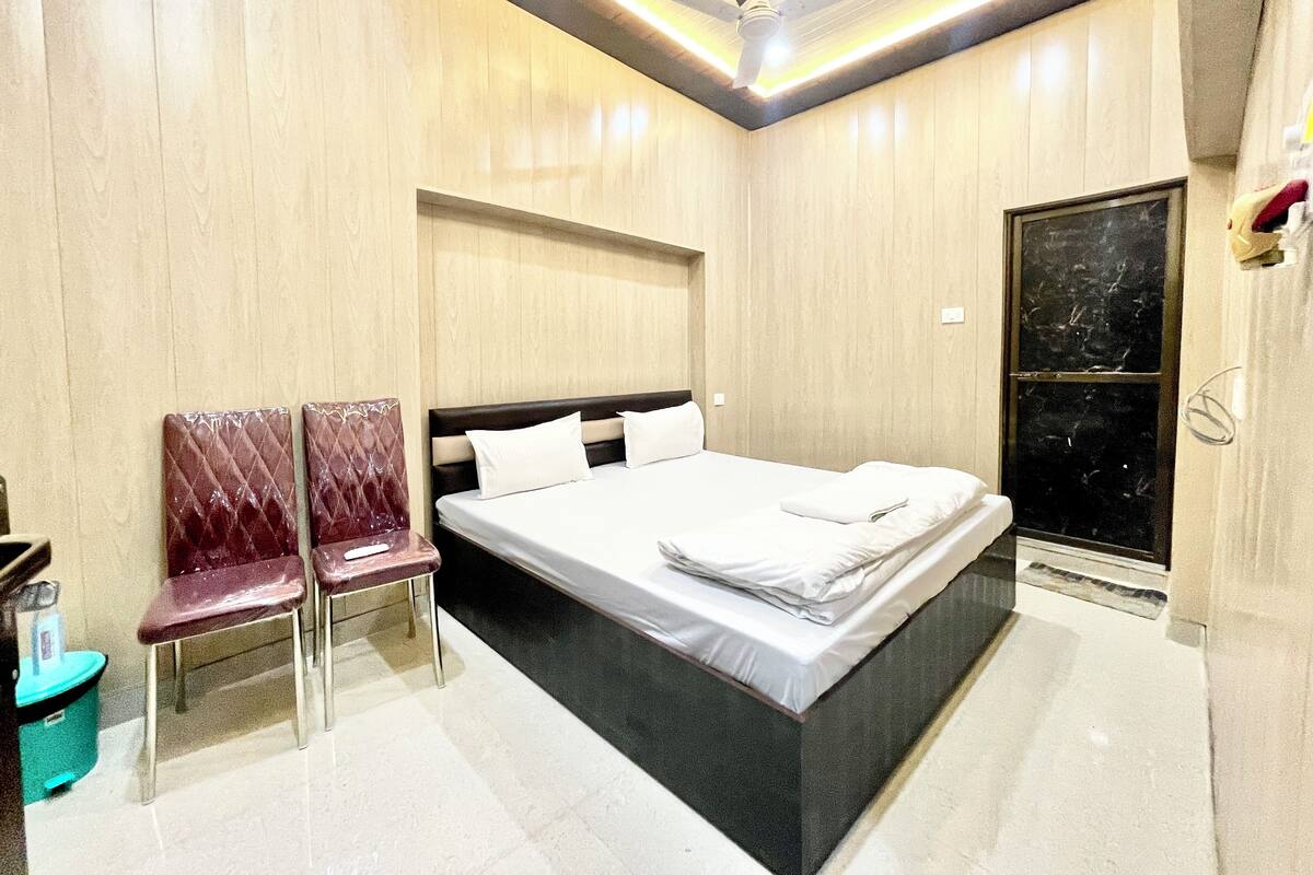 A modern hotel room with a large bed, two chairs, a small table, and a large window.