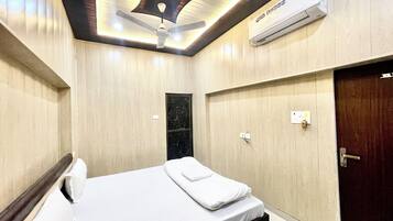 Habitación de hotel con cama, ventilador de techo, equipo de aire acondicionado, una puerta e interruptor de luz.