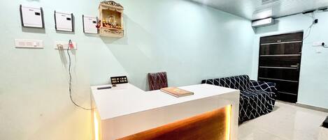 A reception area with a white counter, a small shrine, and a black wardrobe.