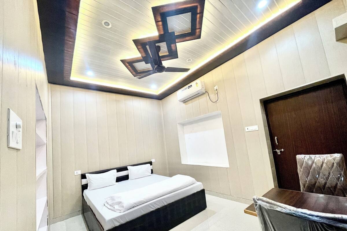 A modern bedroom with a bed, a ceiling light fixture, an air conditioning unit, and a door.