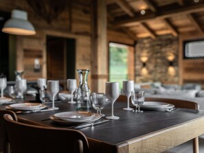 Une table à manger dressée avec des assiettes, des verres et des couverts, dans un intérieur en bois avec un mur en pierre et un luminaire suspendu.