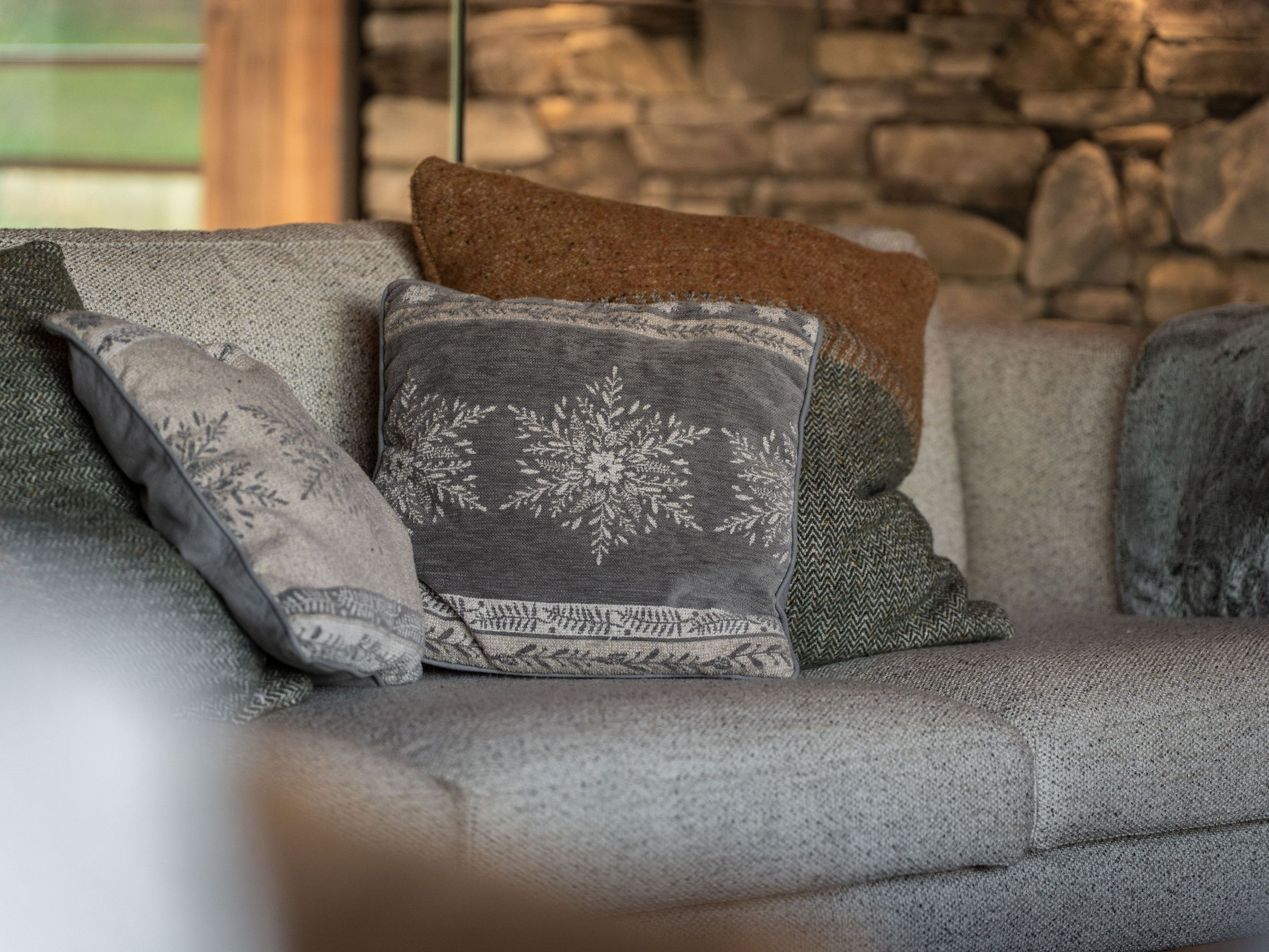 A sofa with multiple cushions, a stone wall in the background, and a hanging light fixture.