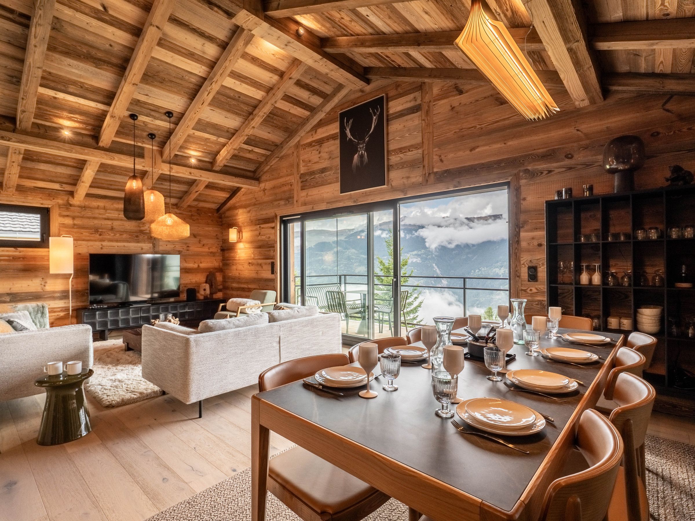 A wooden interior with a dining table set for six, a sofa, and a television.