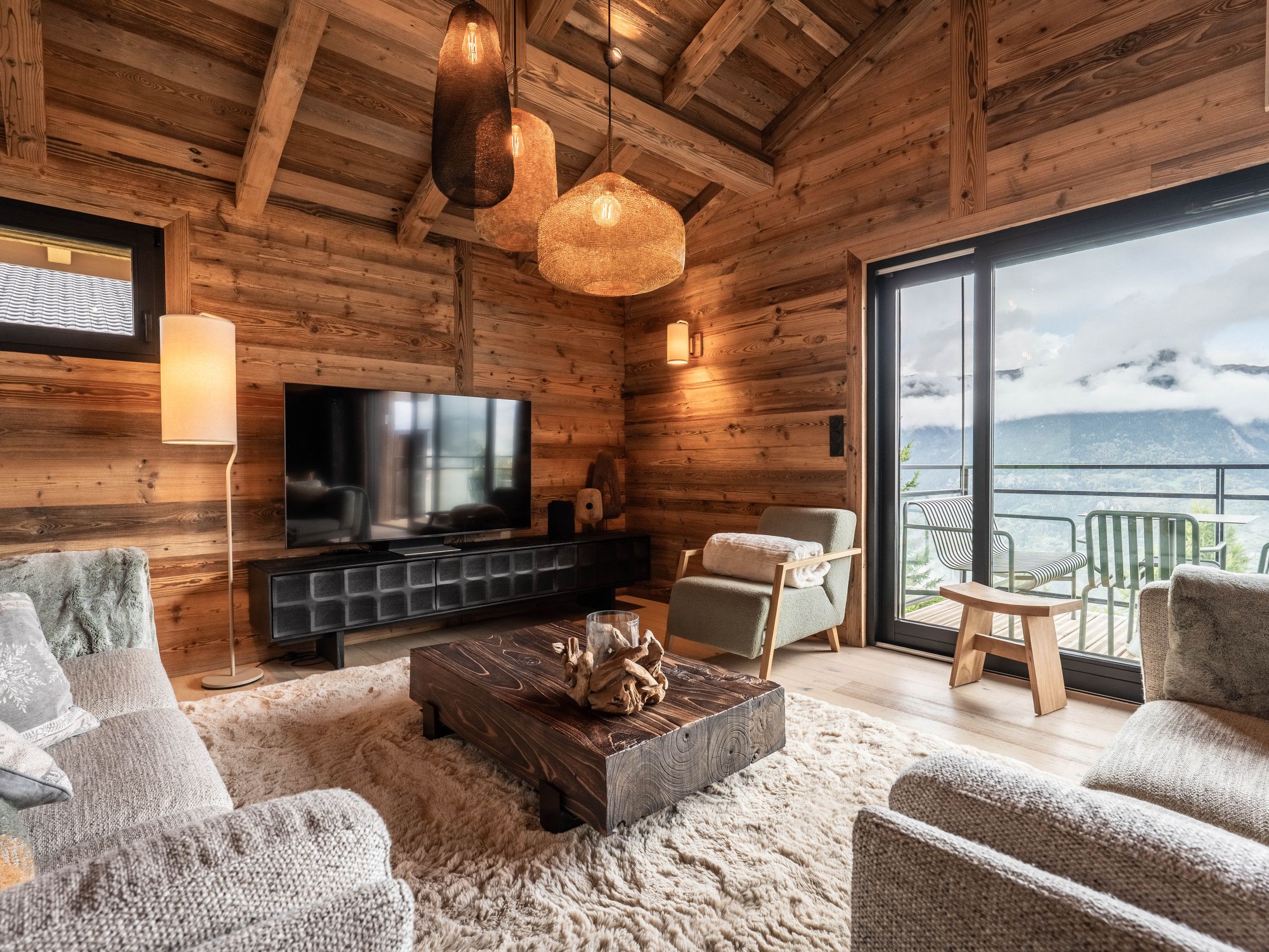 A cozy log cabin interior with a television, seating area, and a balcony with a mountain view.