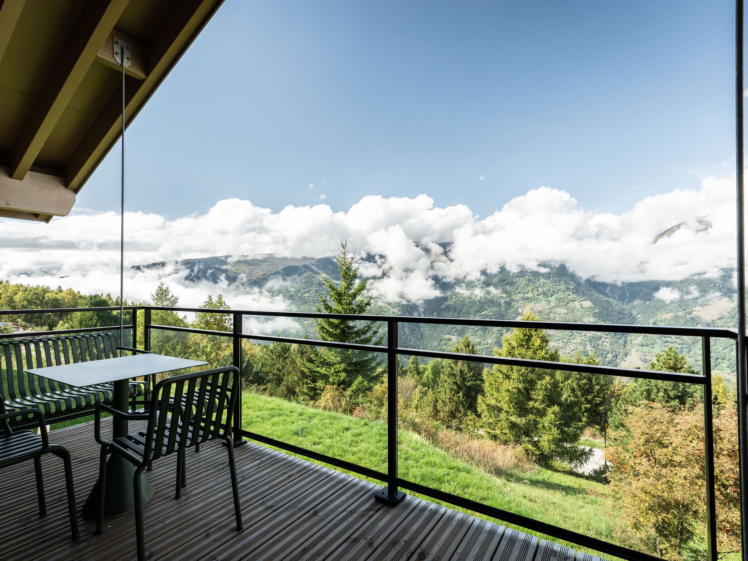 A balcony with a table and chairs, overlooking a mountainous landscape with clouds.