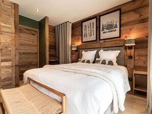 A wooden-paneled bedroom with a large bed, two pillows with animal prints, a bedside table with a lamp, and framed pictures on the wall.