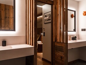 Un baño moderno con detalles de madera, un espejo grande y un lavamanos con dispensador de jabón.
