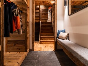 A wooden interior with a bench, a staircase, and a snowboard leaning against the wall.