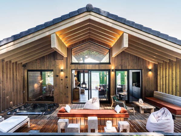 A wooden cabin with a hot tub, outdoor seating, and a view of the outdoors.