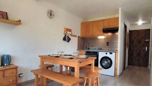 A compact kitchen with wooden cabinets, a washing machine, and a dining area with a wooden table and benches. - Renovated 2-bedroom apartment in Samoëns, pets allowed (Samoëns)