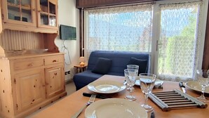 A dining area with a wooden table set for two, a blue sofa, and a cabinet with glass doors. - Renovated 2-bedroom apartment in Samoëns, pets allowed (Samoëns)