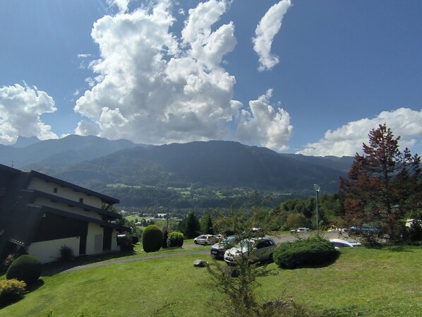 Un quartier résidentiel avec une maison, des voitures garées et une montagne en arrière-plan.