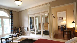 A spacious room with a large bed, a desk, a chair, and a sofa. There is a window with curtains and a view of the outdoors. - 52m² Apt, 4 pers, Casino area, WiFi, Parking (Bagnères-de-Luchon)