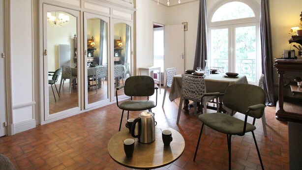 A dining area with a round table, chairs, a chandelier, and a view through a window. - 52m² Apt, 4 pers, Casino area, WiFi, Parking (Bagnères-de-Luchon)