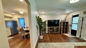 A modern living room with a flat-screen TV, wooden entertainment unit, and a dining area with a table and chairs. - Campus Den on Poplar St. (Marion)