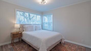 Un dormitorio con cama, mesita de noche, lámpara y alfombra estampada.
