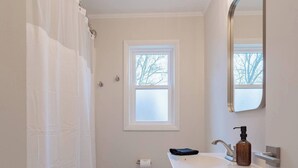 Ein Badezimmer mit Toilette, Waschbecken mit Seifenspender, Fenster und Duschvorhang.