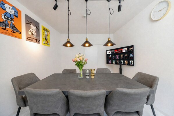 A dining area with a gray table, four gray chairs, hanging pendant lights, a vase with flowers, and a wall clock. - -KISEN- (Osaka)