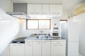 A compact kitchen with white cabinets, a stainless steel sink, a microwave, and a refrigerator. - -KISEN- (Osaka)