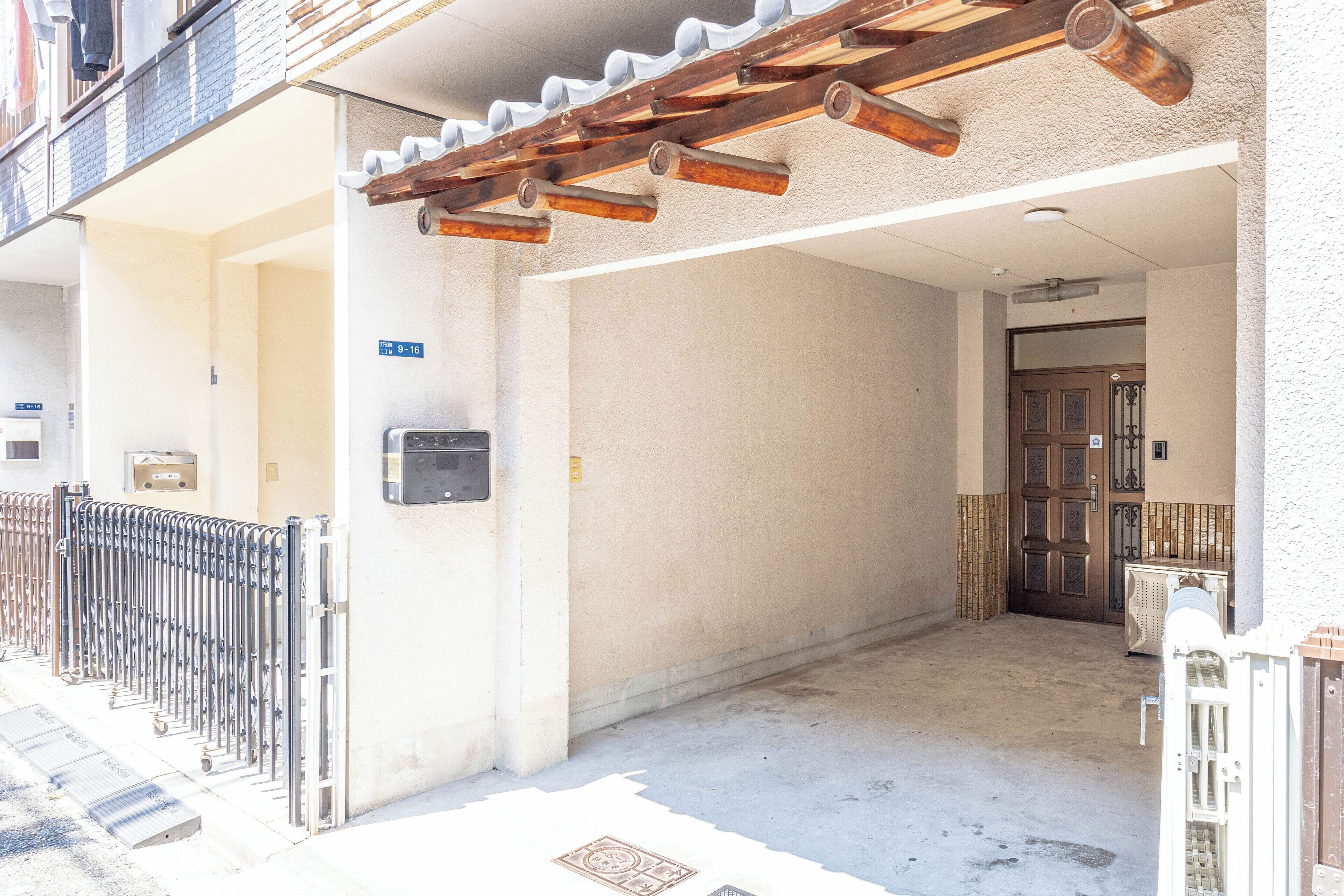 A covered outdoor area with a metal fence, a door, and a wall-mounted intercom.