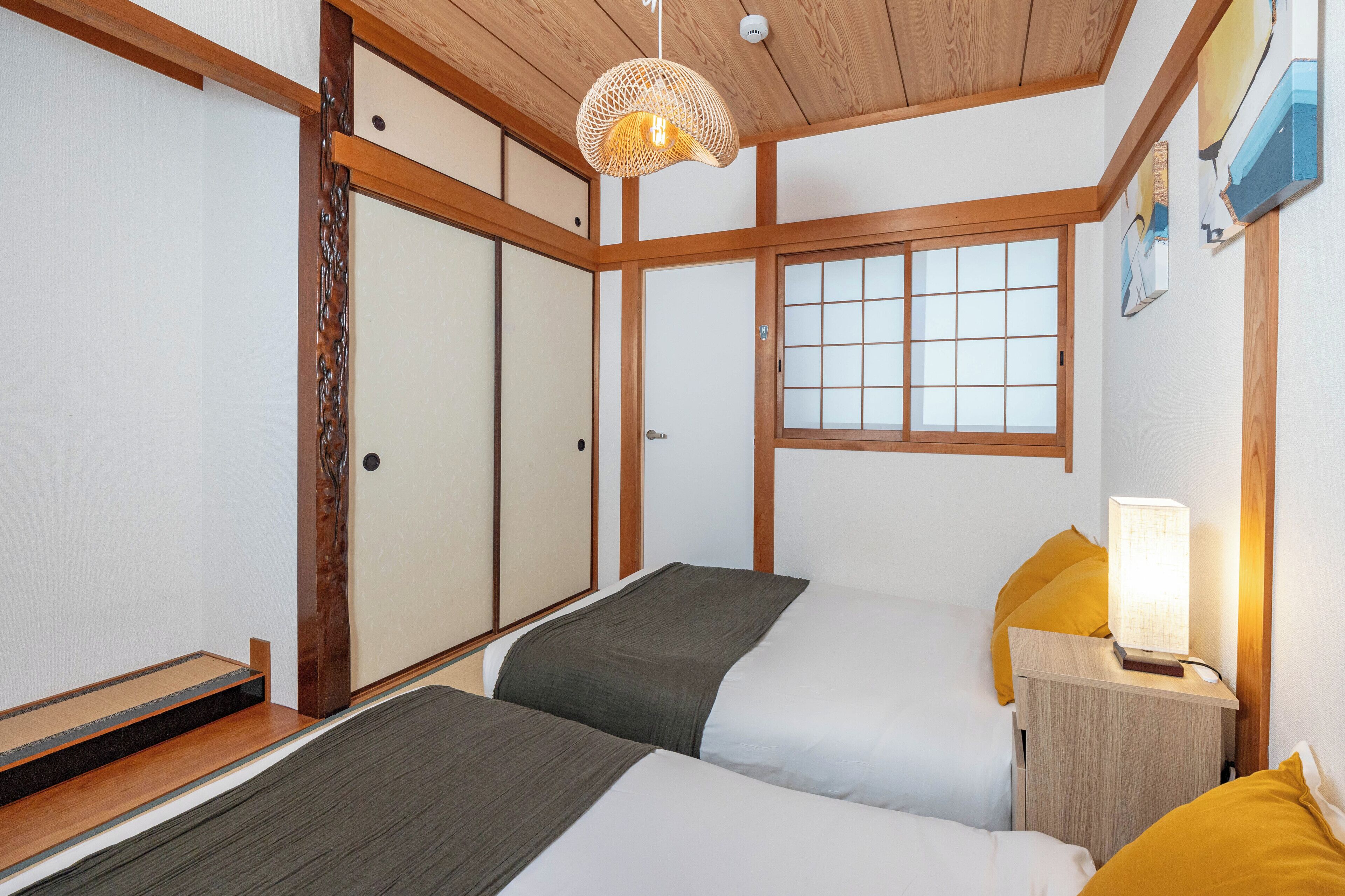A traditional Japanese-style bedroom with two beds, wooden beams, a shoji screen door, and a hanging lamp.