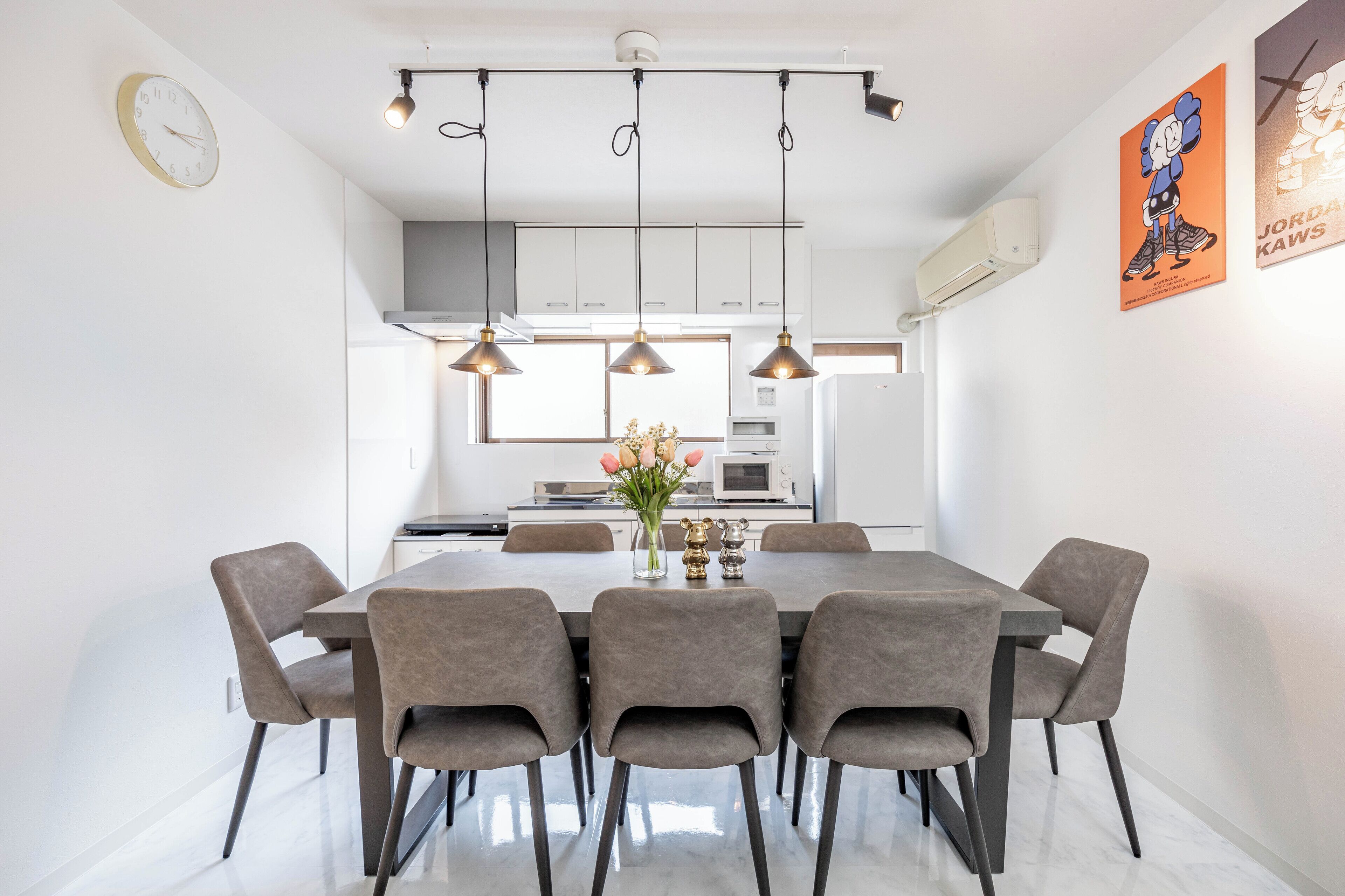A modern dining area with a rectangular table and six chairs, a vase with flowers, and pendant lighting.