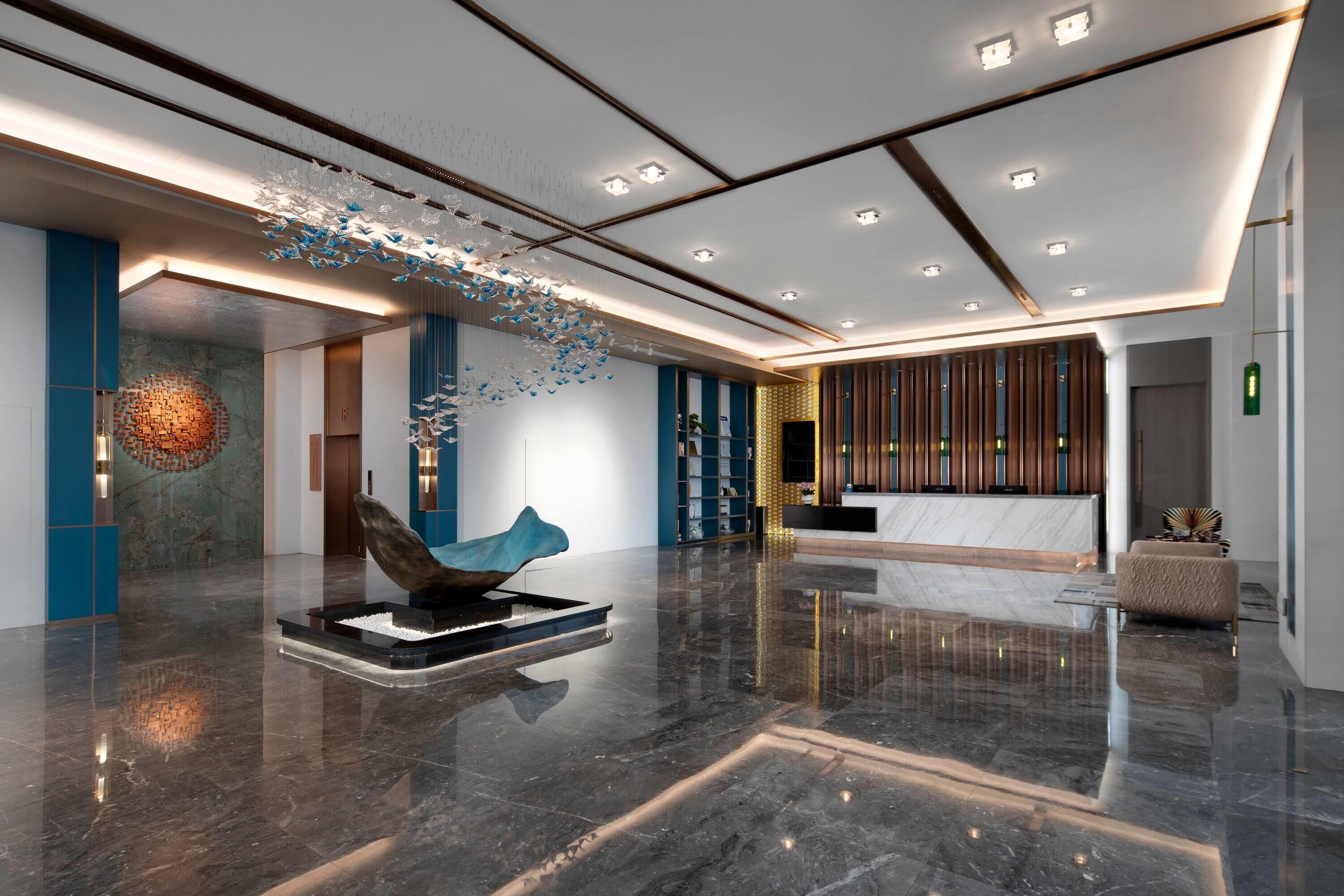 Un hall d’entrée moderne avec un comptoir d’accueil, une sculpture et un mur orné de motifs.