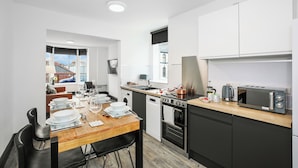 A modern kitchen with white cabinets, a wooden dining table, and a view of the city. - TYME Suites on Humber (Cleethorpes)