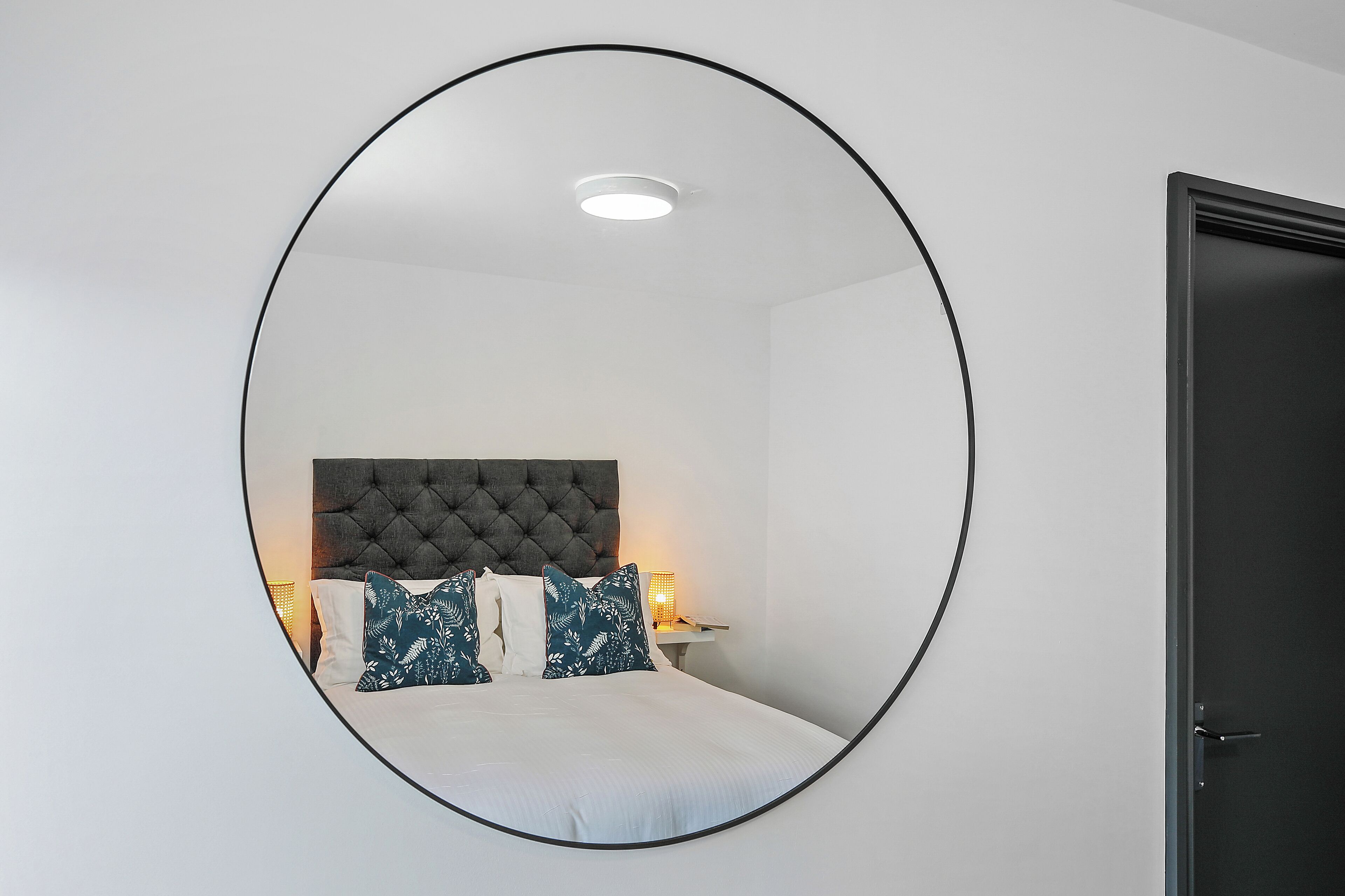 A bedroom with a tufted headboard, a bed with white bedding, and a bedside table with a lamp.