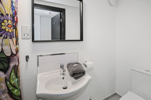 A bathroom with a white sink, a mirror, and a toilet. - TYME Suites on Humber (Cleethorpes)