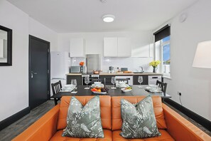 A modern kitchen with white cabinets, a dining table set with plates, glasses, and a fruit bowl. - TYME Suites on Humber (Cleethorpes)