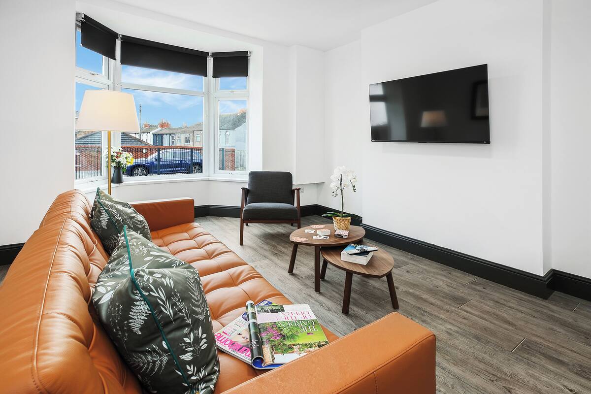 A modern living room with a leather sofa, a dining table, and a TV mounted on the wall.