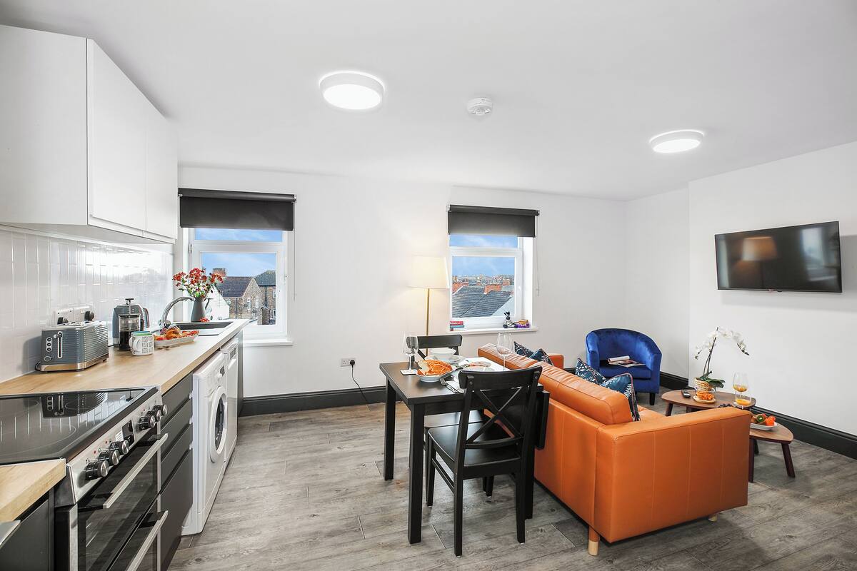 A modern kitchen with a dining area, a sofa, and a TV.