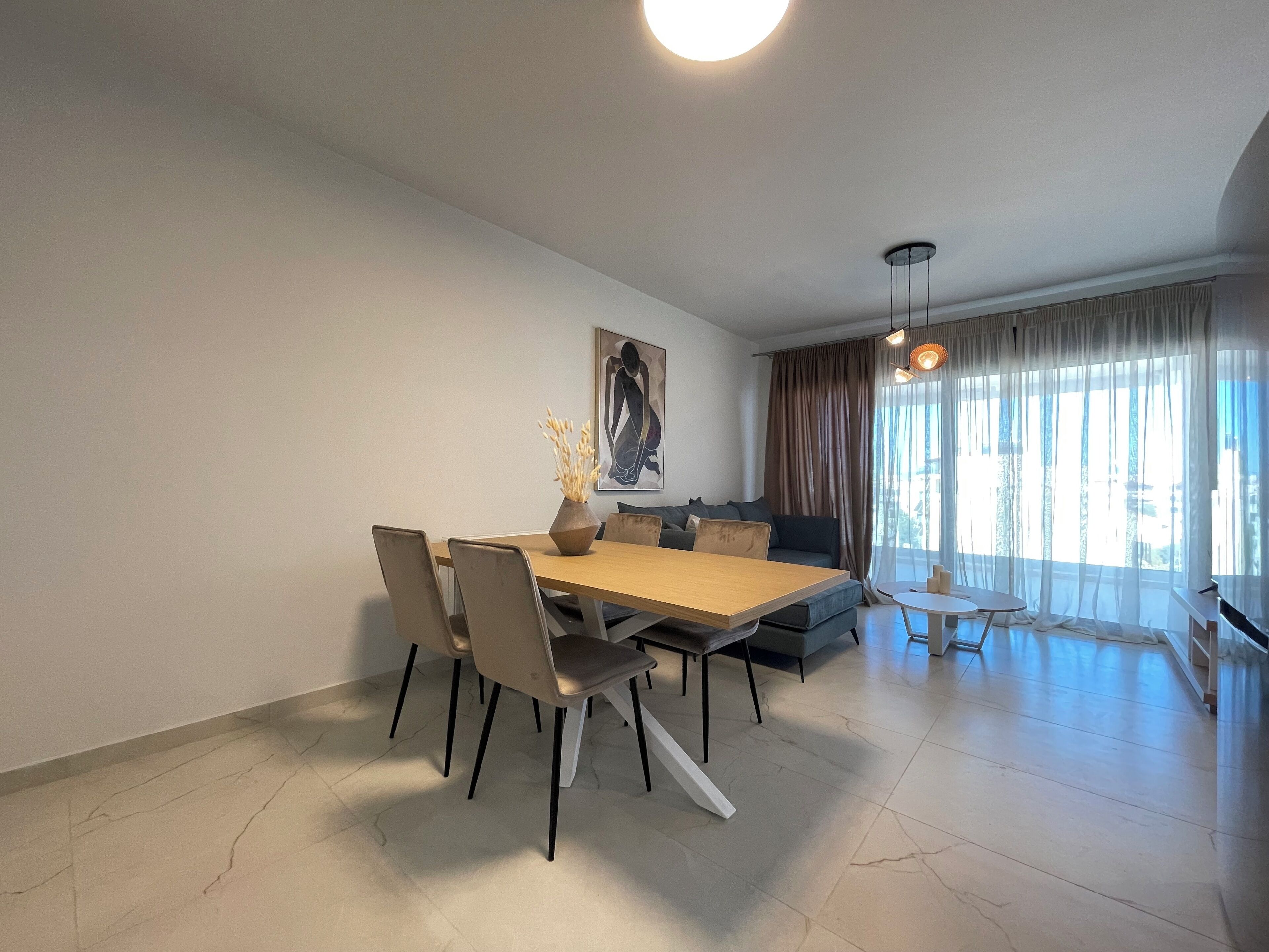 A modern living room with a dining area, featuring a sofa, a coffee table, and a dining table with chairs.