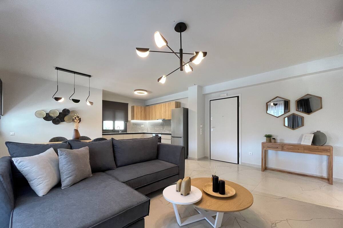Una sala de estar moderna con un sofá gris, una mesa de centro redonda y una cocina al fondo.