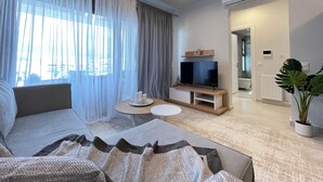 Een moderne woonkamer met een bank, een televisie op een houten dressoir, een ronde tafel met kaarsen, en een kamerplant.
