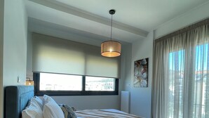 Een moderne slaapkamer met een groot bed, een hanglamp, een raam met gordijnen en uitzicht op het buiten.