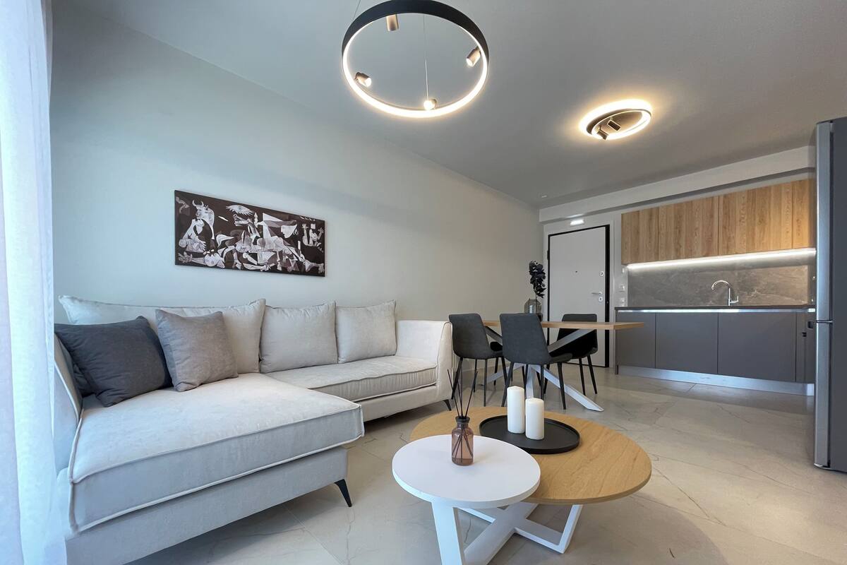 Una sala moderna con un sofá gris, una mesa de centro redonda y un comedor con una mesa y sillas de madera.