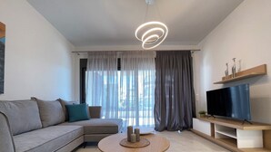 Un salon moderne avec un canapé, une table basse ronde, un téléviseur à écran plat posé sur un meuble en bois et un luminaire suspendu au plafond.